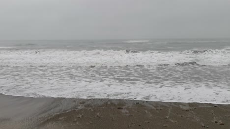 Movement-of-waves-on-a-ocean-sore-with-stormy-weather,-mist-covering-sky