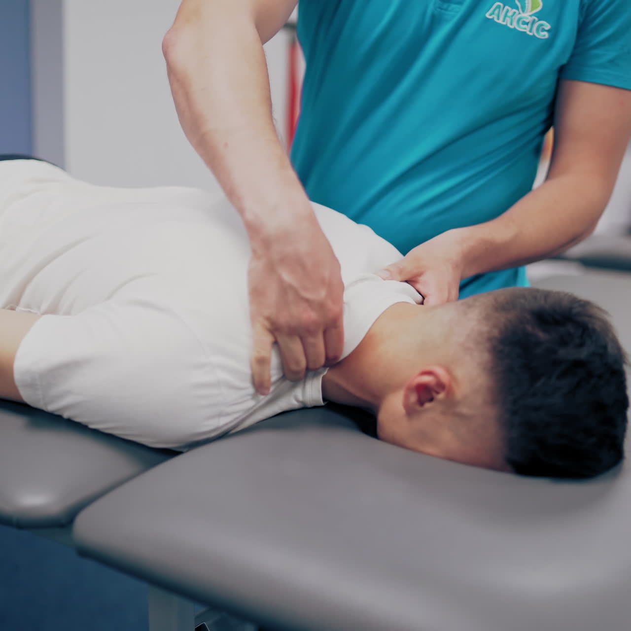 Man in white t-shirt is having a neck massage in spa center. Professional massagist is doing therapy treatment on a man's body indoors.