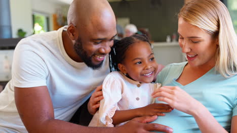 family with daughter cuddling pregnant mother at home together