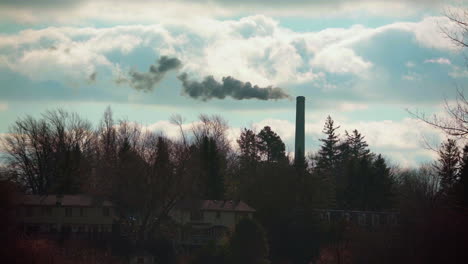 wide angle of a smoke stack spewing dark thick smoke into the sky on a beautiful day