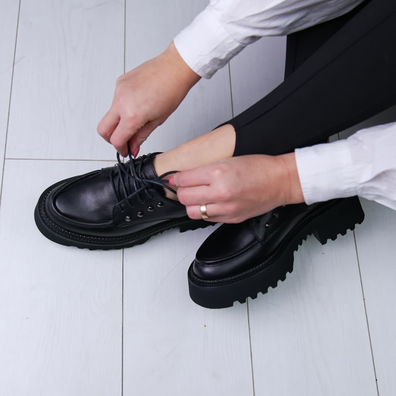 Demonstration of modern black shoes with laces and massive soles. Lady in black leggings and white shirt showing the fashionable footwear in studio. White backdrop