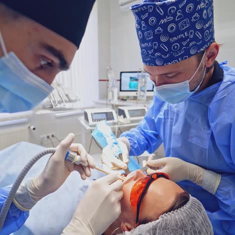 modern stomatology cabinet. dentist together with his assistant in protective uniform treating patient's teeth in dental office.
