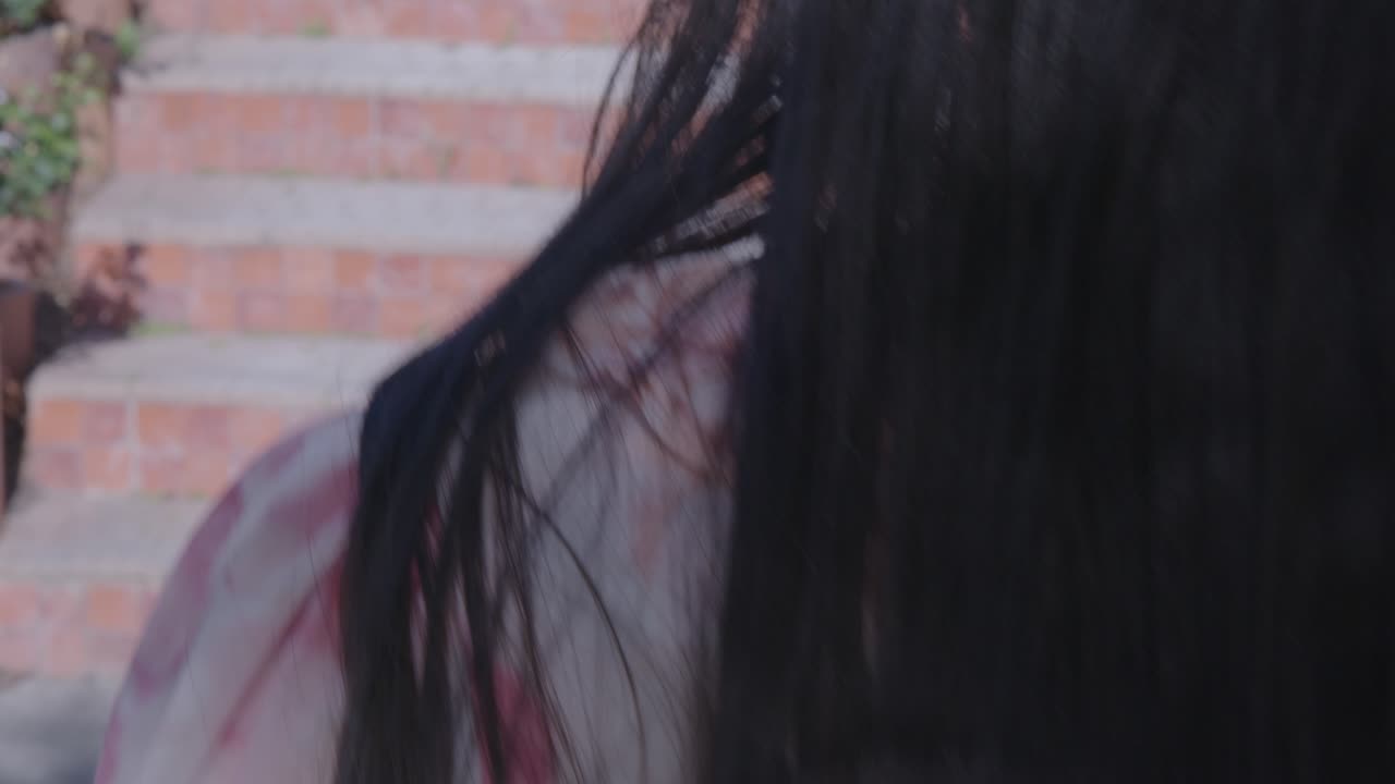A girl with long hair in a floral dress gracefully walks down stone steps in a sunlit garden. The soft afternoon light casts gentle shadows, creating a tranquil, serene ambiance