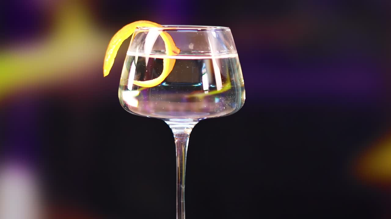 Un bicchiere da martini con una scorza di limone ruota su uno sfondo vibrante e sfocato con illuminazione dinamica.