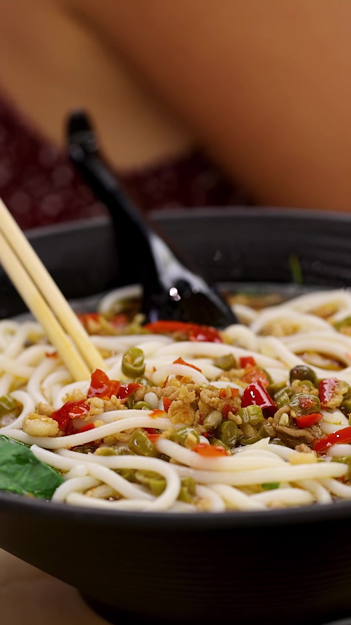 Movimento lento della telecamera intorno a una ciotola di zuppa di noodles piccante e calda sotto l'illuminazione calda di un ristorante.