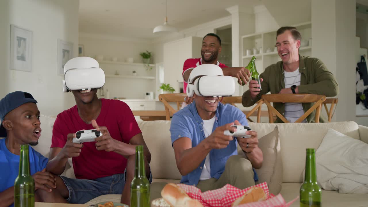Amici di diverse etnie che giocano alla realtà virtuale a casa, uno che indossa il visore e manovra i controller con delle birre.