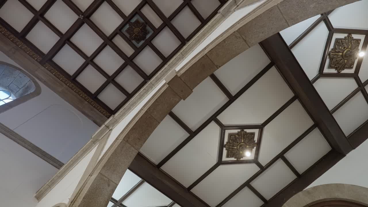 Vista angolata verso l'alto dell'interno di una chiesa che mostra un arco in pietra e pannelli geometrici in legno del soffitto a cassettoni con un dettaglio decorativo centrale