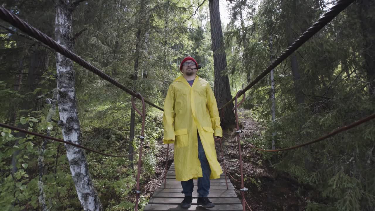 Man in Yellow Raincoat Crossing a Forest Bridge
