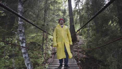 man in yellow raincoat crossing a forest bridge