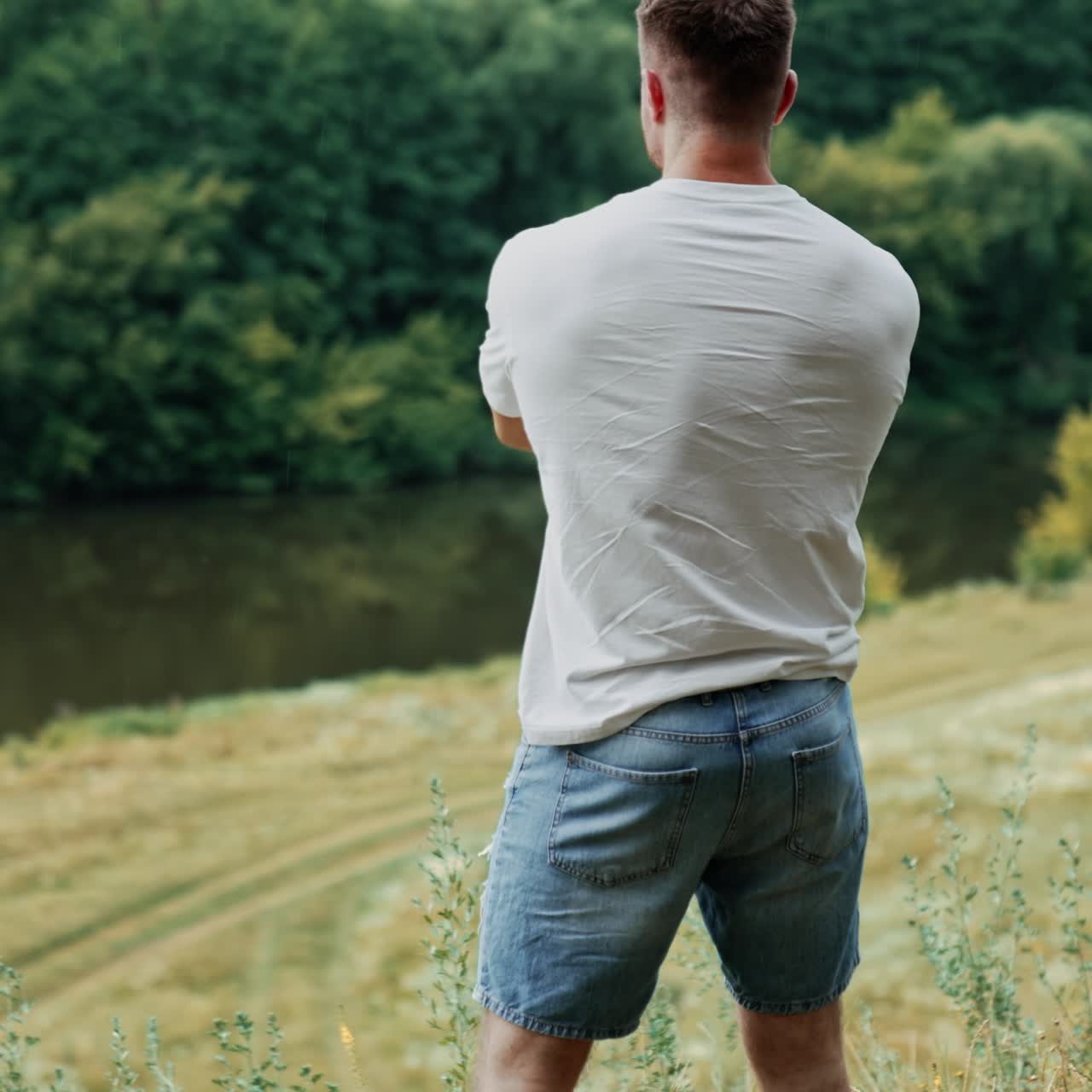 Vista posteriore di un uomo sportivo e muscoloso in t-shirt bianca e pantaloncini di jeans. Persona felice immersa nella natura che si gode la vita