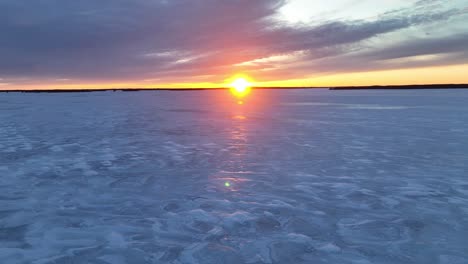 Flying-away-from-the-sun-during-sunset,-over-a-frozen-lake