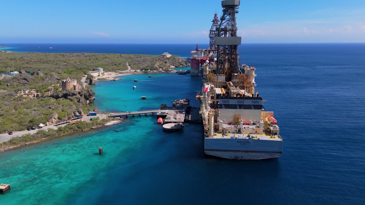 Scenic aerial pullback of Fort Beekenburg with oil drilling rig platform ship in the background, clear ocean waters surrounding