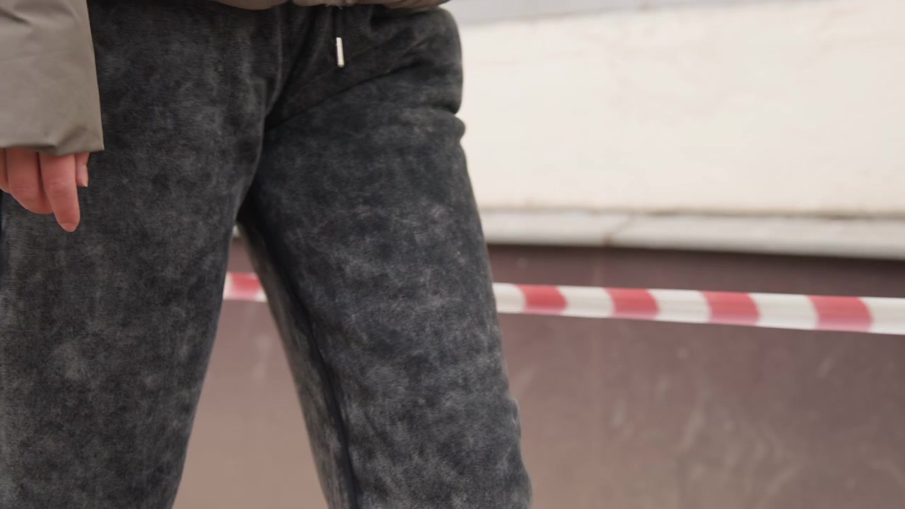 City woman beside barrier tape calmly. Individual in gray attire awaits near construction barrier. Urban environment features woman standing calmly next to caution tape by sidewalk