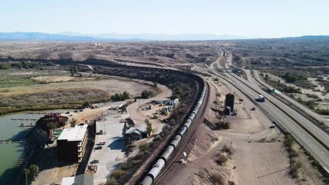 Largo-Tren-De-Carga-Que-Transporta-Carga-A-Través-Del-Desierto,-Frontera-Entre-California-Y-Arizona,-Río-Colorado,-Autopista-I-40-Este,-Toma-Aérea-Cinematográfica-De-Gran-Angular