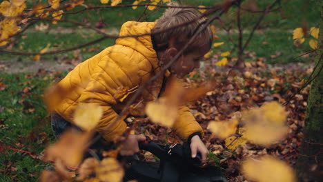 young boy in yellow coat uses electric leaf blower on lawn