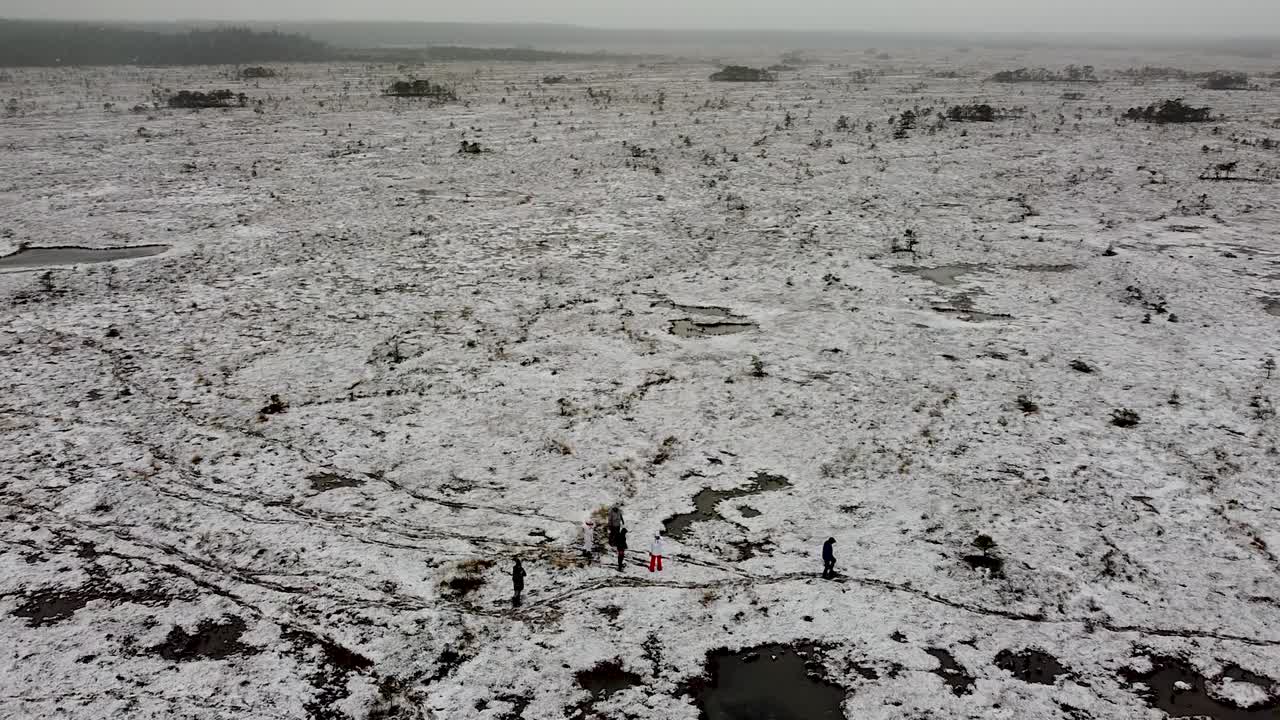 전경에서 눈신을 신고 걷는 사람들과 함께 탁 트인 늪지 풍경을 회전하는 공중 드론 보기