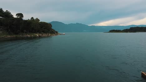 Drone-aerial-flying-over-a-man-paddling-on-a-boat-in-beautiful-Lake-Atitlan,-Guatemala