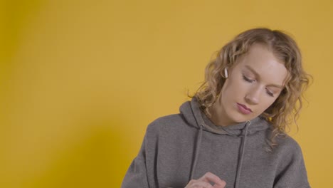 Foto-De-Estudio-De-Una-Joven-Escuchando-Música-En-El-Teléfono-Móvil-Y-Bailando-Con-Fondo-Amarillo