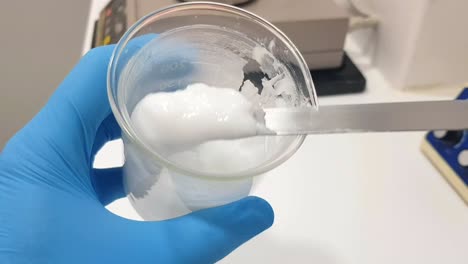 close-up footage of a beaker containing a white emulsion being stirred with a spatula. the creamy substance is mixed thoroughly,