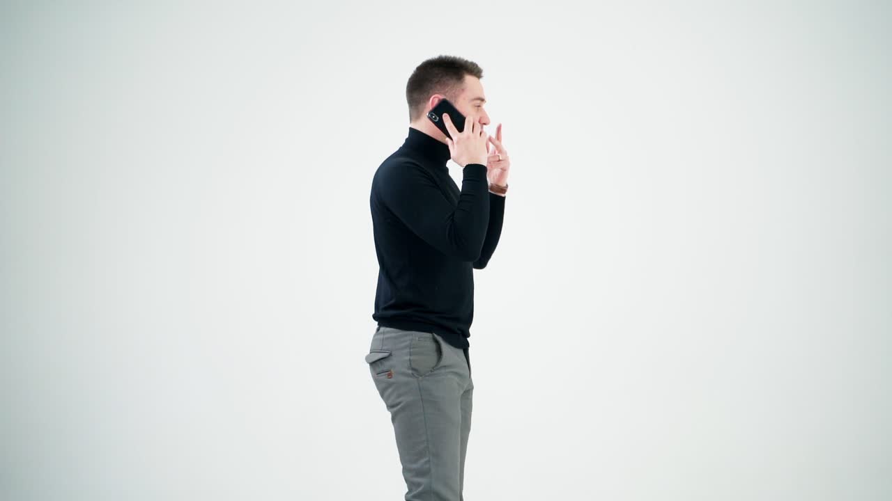 Young businessman talking on the phone. Handsome man in black sweater and grey trousers leading e-business through the cellphone. Man isolated on white.