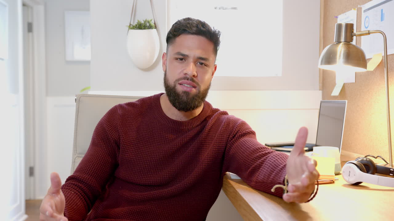 Talking and gesturing on video call, man sitting at desk in home office setting