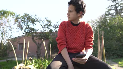 frustrated young man with scarred face typing on phone in outdoor setting