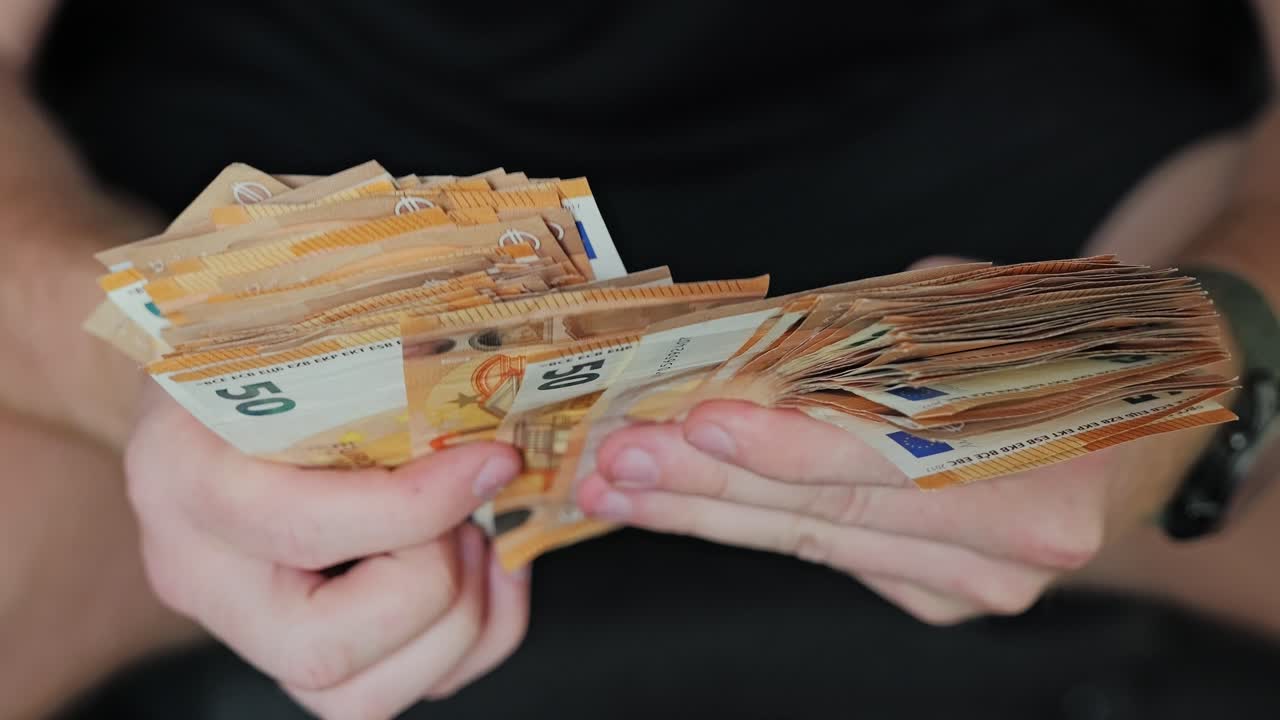 Seated man counts thick stack of euros in slow motion from front camera