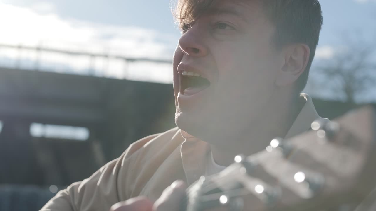 바위의 배경에 산의 강변에 앉아 기타를 연주하는 젊은이. 자유의 개념, 휴식 장소.