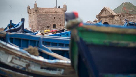 la cámara se desliza hacia la izquierda con barcos de pesca borrosos en primer plano y la entrada de la fortaleza y el puerto en foco en essaouira, marruecos