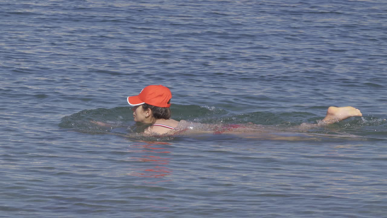 Pregnant woman in a red swimming suit moving around in the Mediterranean sea