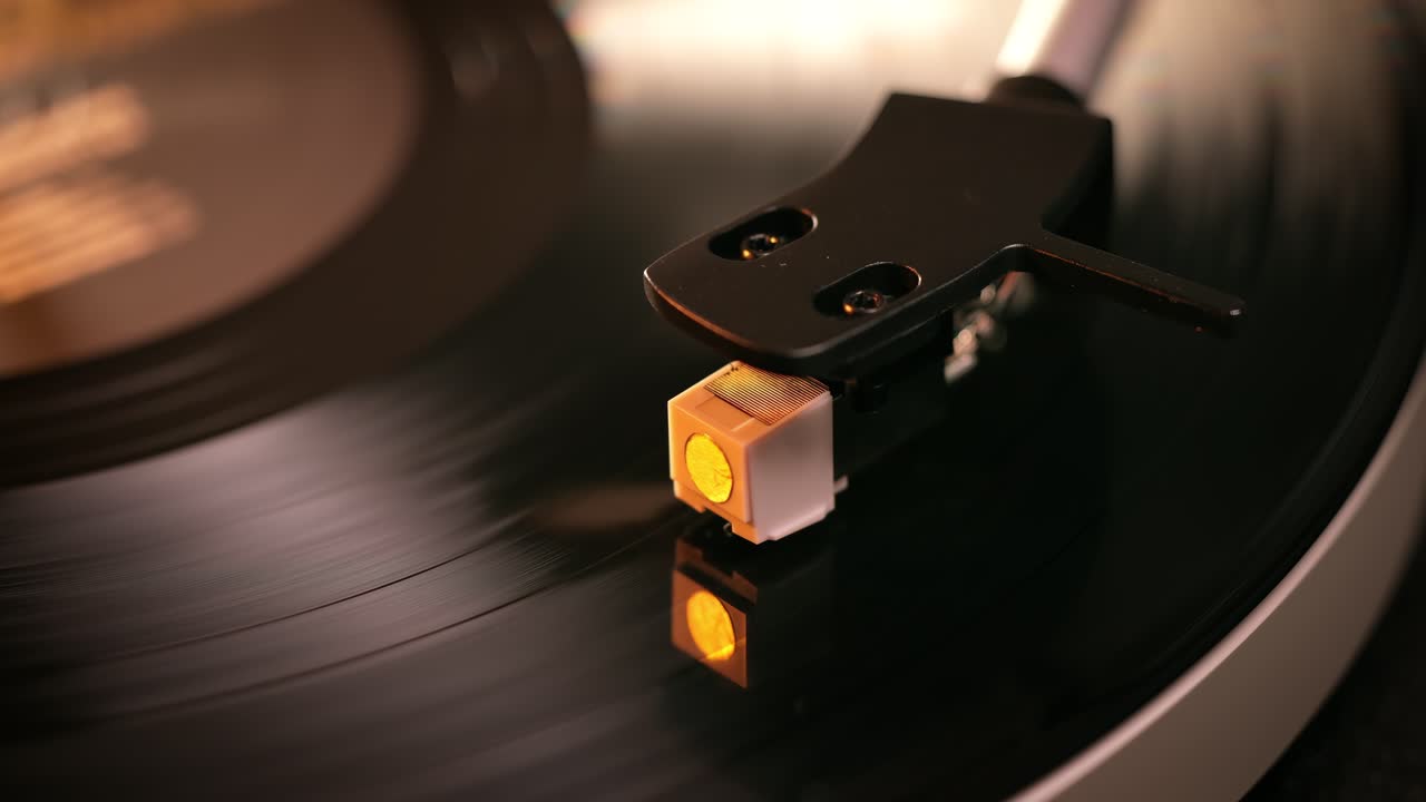 Primo piano dettagliato del braccio di un giradischi con testina bianca, posizionato su un disco in vinile nero sul piatto, che evidenzia la precisione delle apparecchiature audio