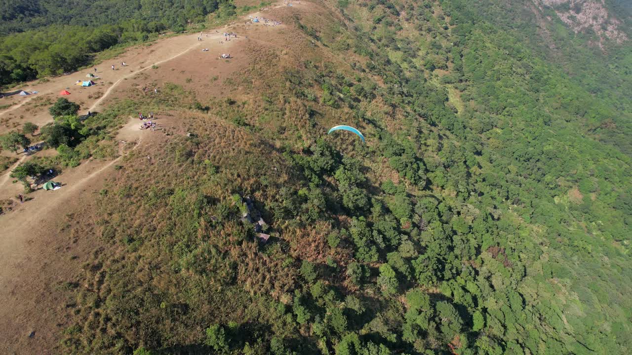 parapente en un paracaídas azul sobrevolando ngong ping en hongkong mientras la sombra se mueve sobre la vegetación verde