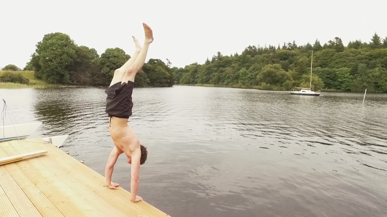젊은 남자는 부두에서 강으로 물구나무서기 다이빙을 수행합니다.