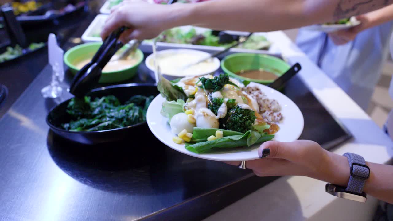 Close-up of diner adding cooked spinach to colorful salad plate at self-service buffet