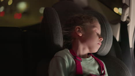 una vista de cerca de un niño durmiendo pacíficamente en un asiento de coche por la noche, el niño está usando un mono rosa y una camisa verde claro, descansando cómodamente contra el asiento del coche