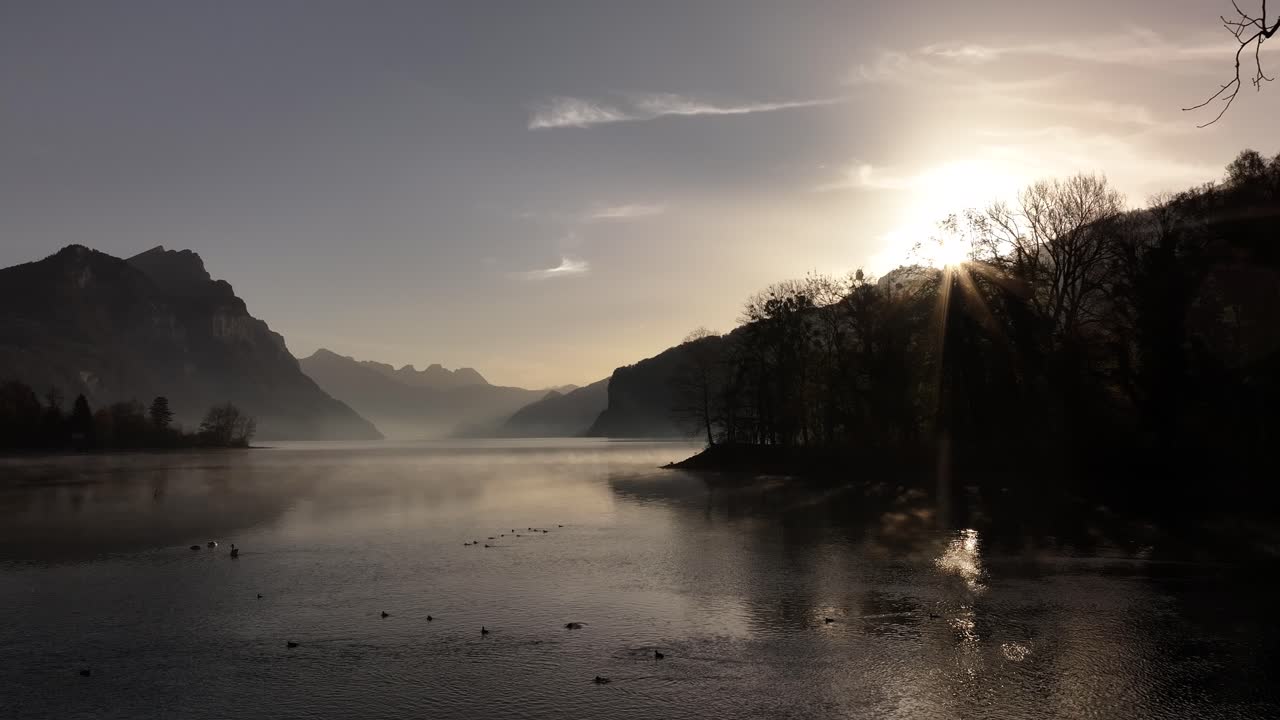 mañana tranquila en walensee, suiza, con vistas nebulosas al lago, rayos de sol sobre las montañas y cámara lenta, belleza tranquila del paisaje suizo.