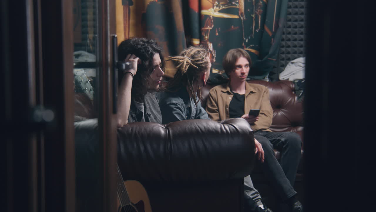 la banda de rock musical se sienta en el sofá. jóvenes músicos masculinos, artistas, intérpretes escuchan canciones terminadas grabadas para un nuevo álbum en un estudio profesional de grabación de sonido y música. concepto de producción musical.