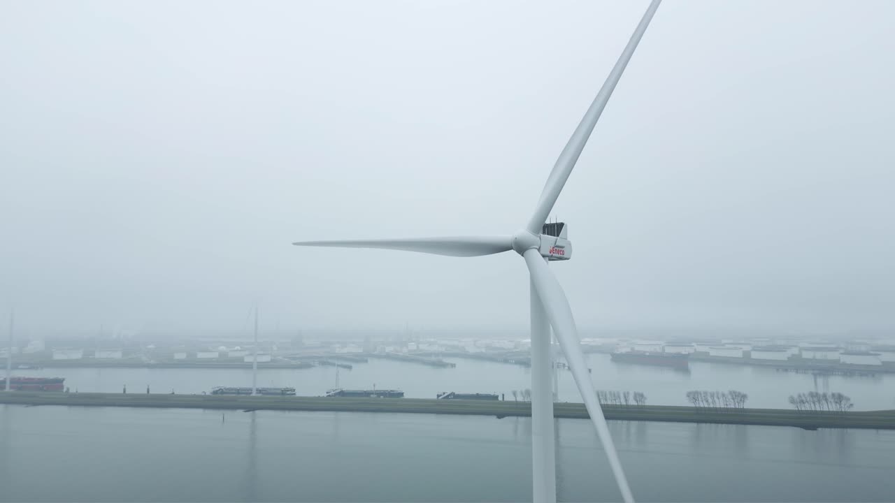 Ripresa con drone di una grande turbina eolica in funzione vicino alle acque di un porto industriale - Hoek van Holland.