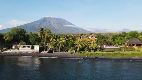 panning drone view of the impressive mount agung volcano towering above the coastal town of tulamben bali