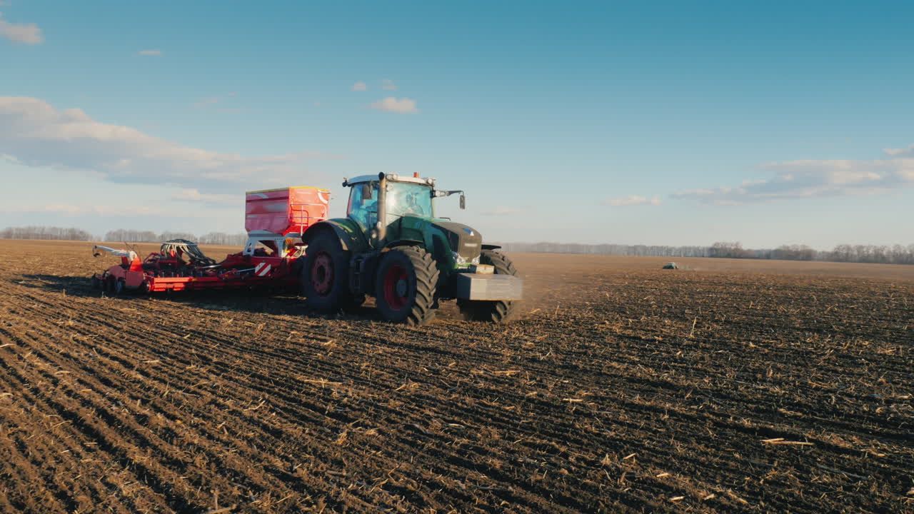 스테디캠 팬 샷: 초봄에 밭에 밀을 뿌리는 파종기가 있는 트랙터 1