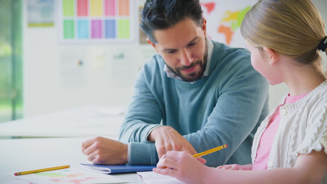 maestro de sexo masculino con estudiante de sexo femenino en el aula de la escuela sentado en el escritorio escribiendo en el libro juntos