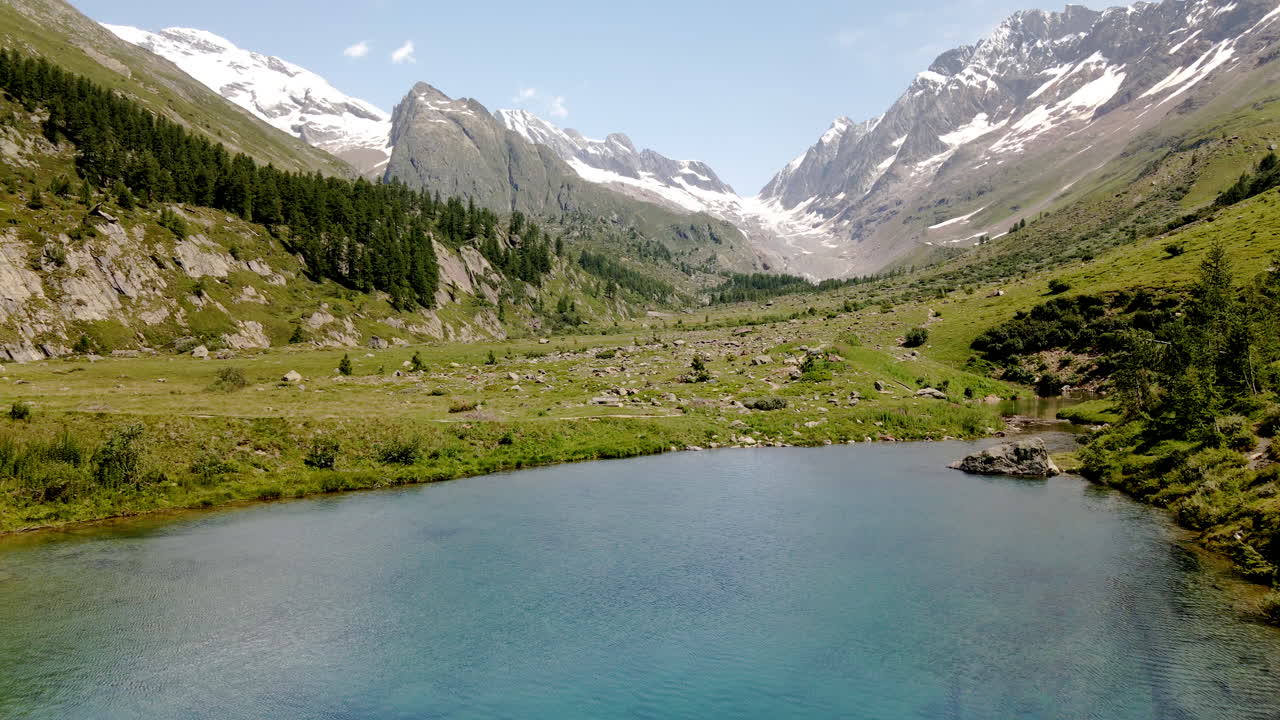 vista aérea avanzando a través de un lago de montaña de agua turquesa clara en el verano, con montañas nevadas en el fondo
