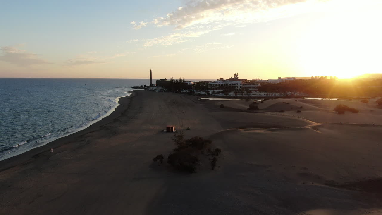 Drone flying low and rotating over a sandy beach during sunset
