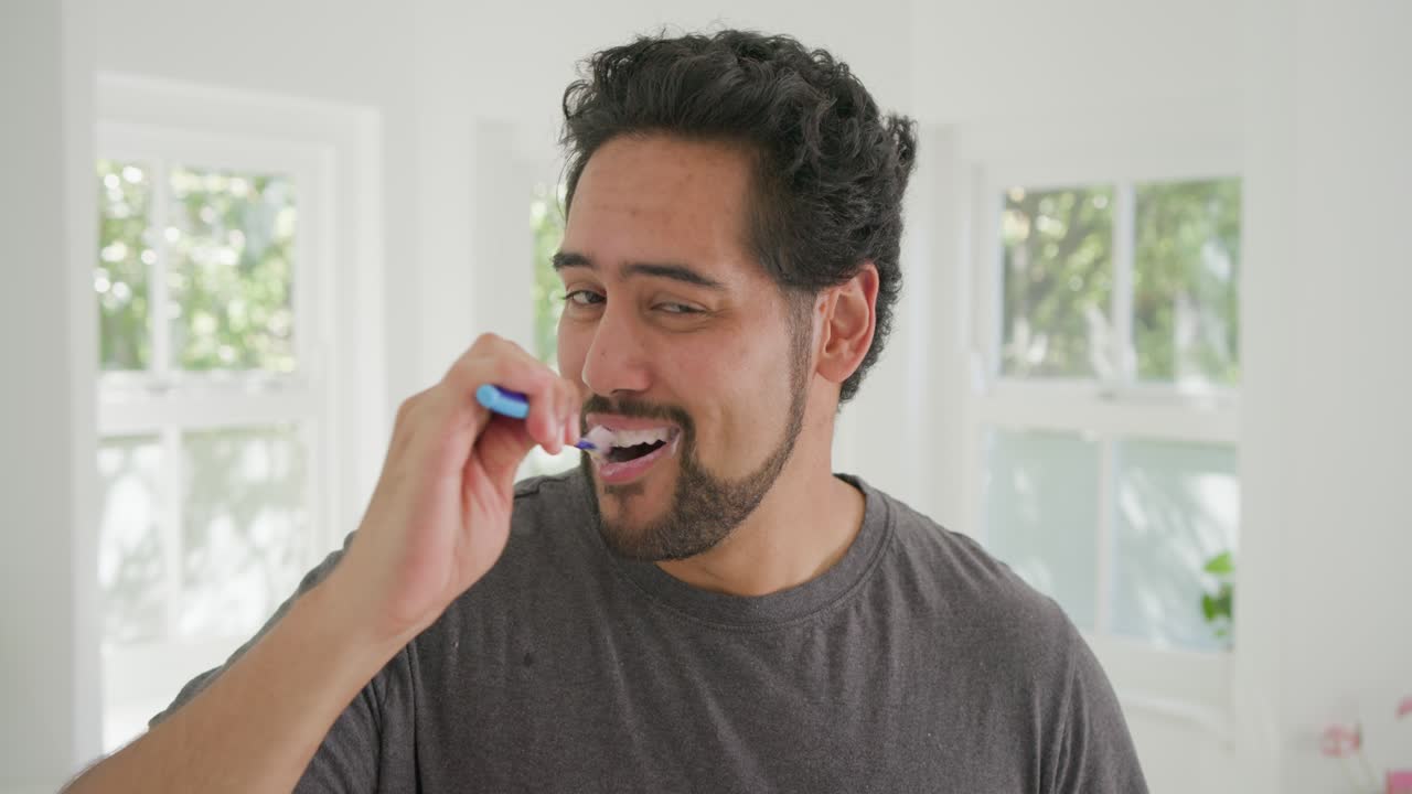 Mid-adult African American man raising blue-handled toothbrush brushing teeth for care in bathroom