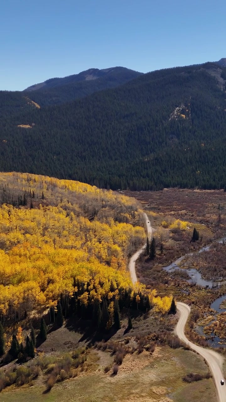 Ripresa verticale con drone di un passo di montagna, un ruscello e colori autunnali nel paesaggio del Colorado, USA, scenario panoramico in una soleggiata giornata autunnale
