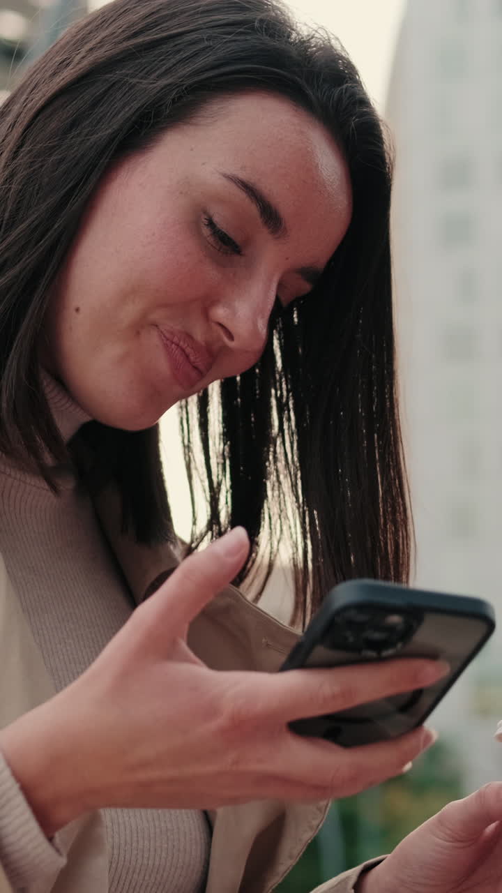 Giovane donna sorridente mentre usa lo smartphone e tiene in mano un caffè