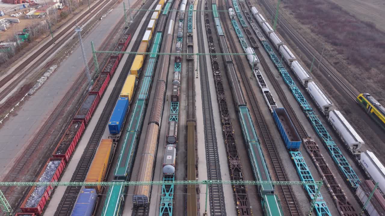 Luftaufnahme eines großen Rangierbahnhofs, gefüllt mit Güterzügen und Güterwaggons, die auf parallelen Gleisen angeordnet sind. Das Video zeigt modernen Schienenverkehr, Logistikabläufe und Güterverteilung