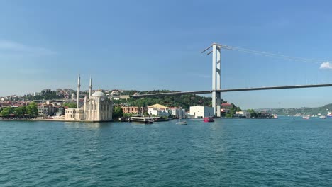 footage of boats passing on bosphorus, historical landmark called "ortakoy mosque" and bridge in istanbul. it is a beautiful scene in a sunny summer day.