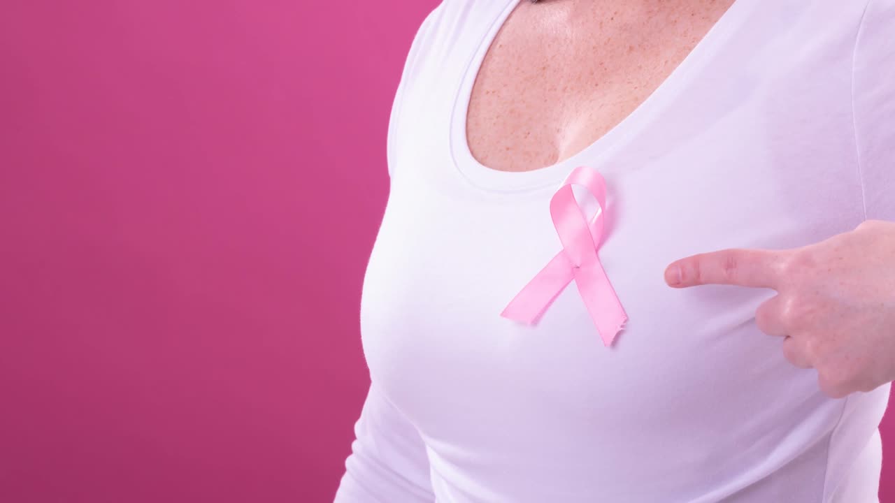 Video del mezzo busto di una donna caucasica che indossa un nastro rosa per la sensibilizzazione al cancro, con sfondo rosa.