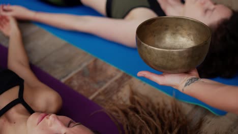 female hands holding singing bowl over heads of yoga class participants